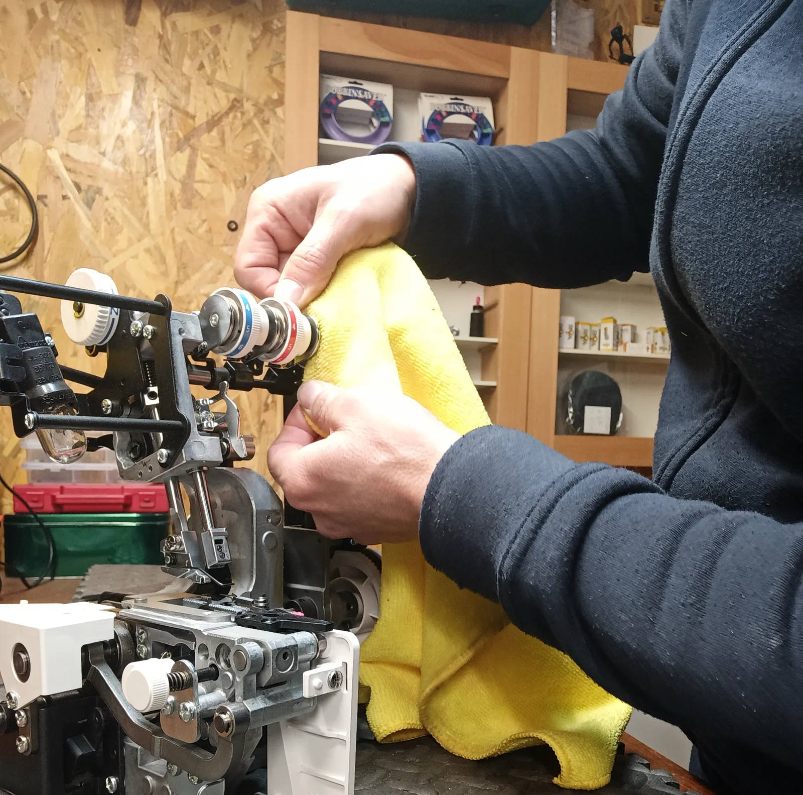 Un réparateur règle les tensions d'une surjeteuse, tissu jaune en main, dans son atelier.