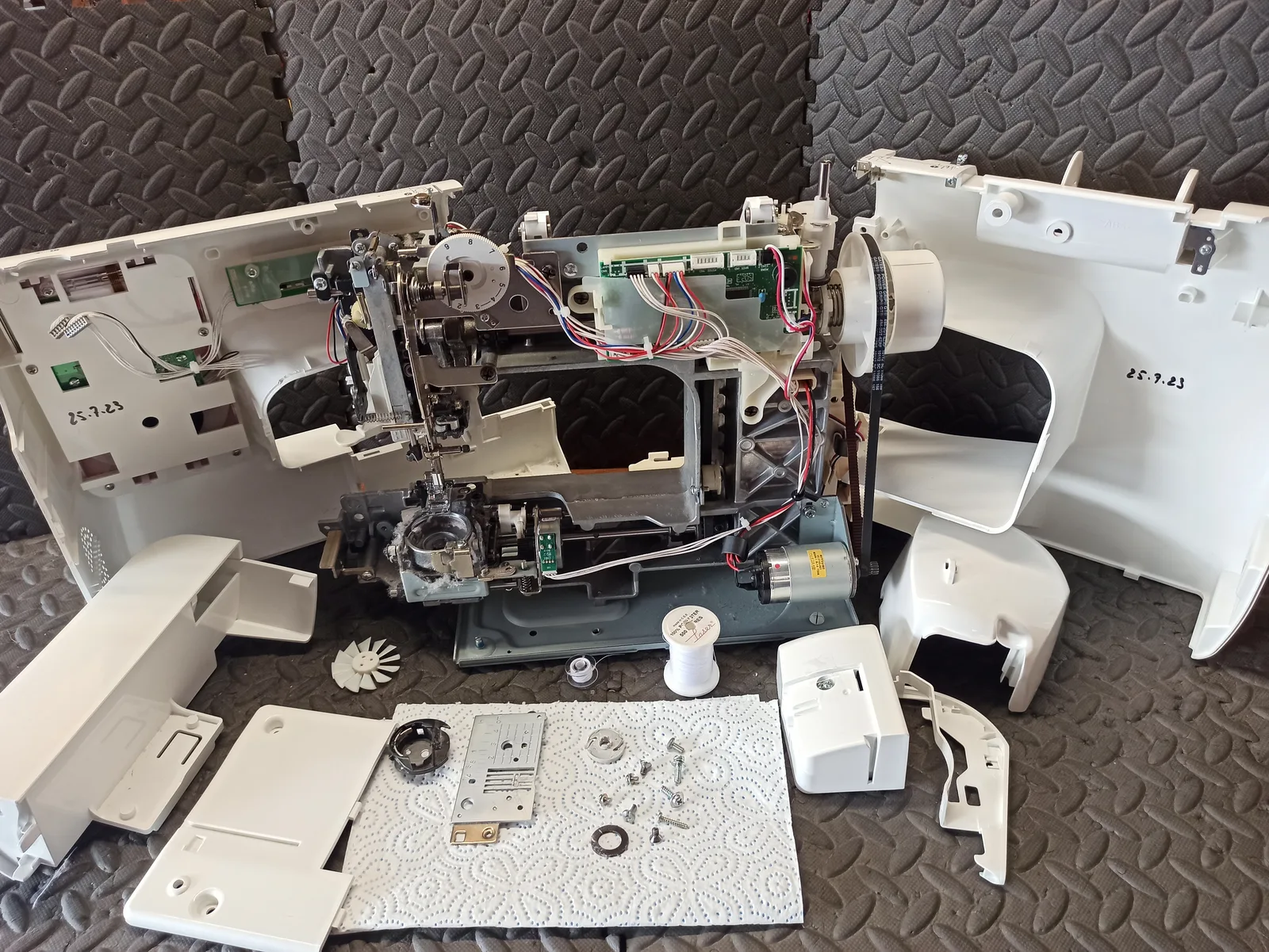 Machine à coudre entièrement démontée pour révision, pièces et carte électronique posées sur l'établi.